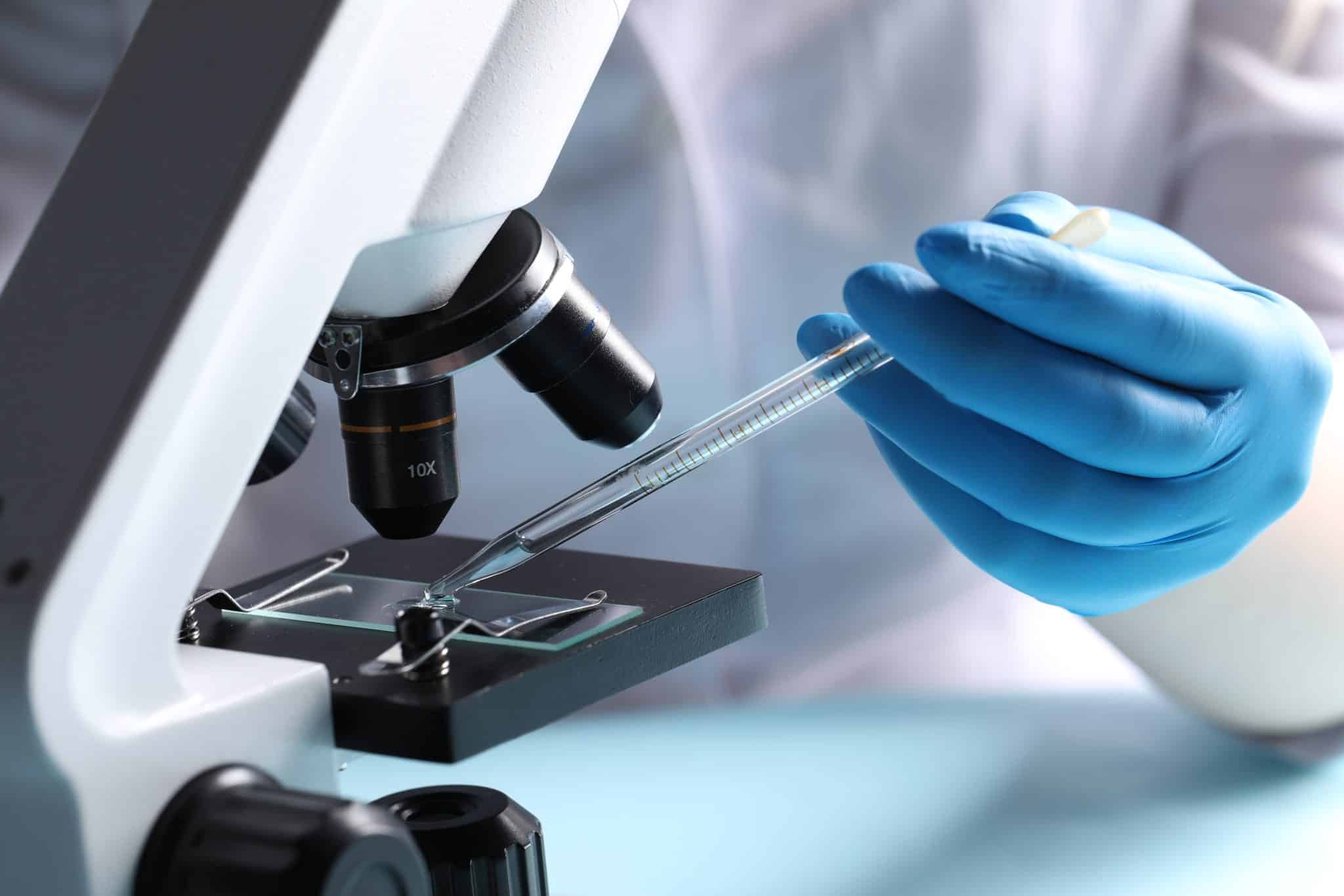 doctor,dripping,liquid,from,pipette,onto,glass,slide,on,microscope,